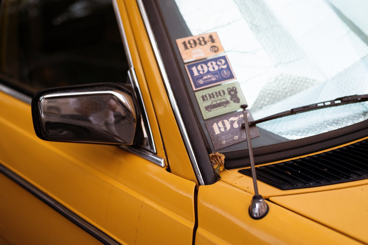 Close-up of a classic yellow car with retro decade stickers on the windshield.