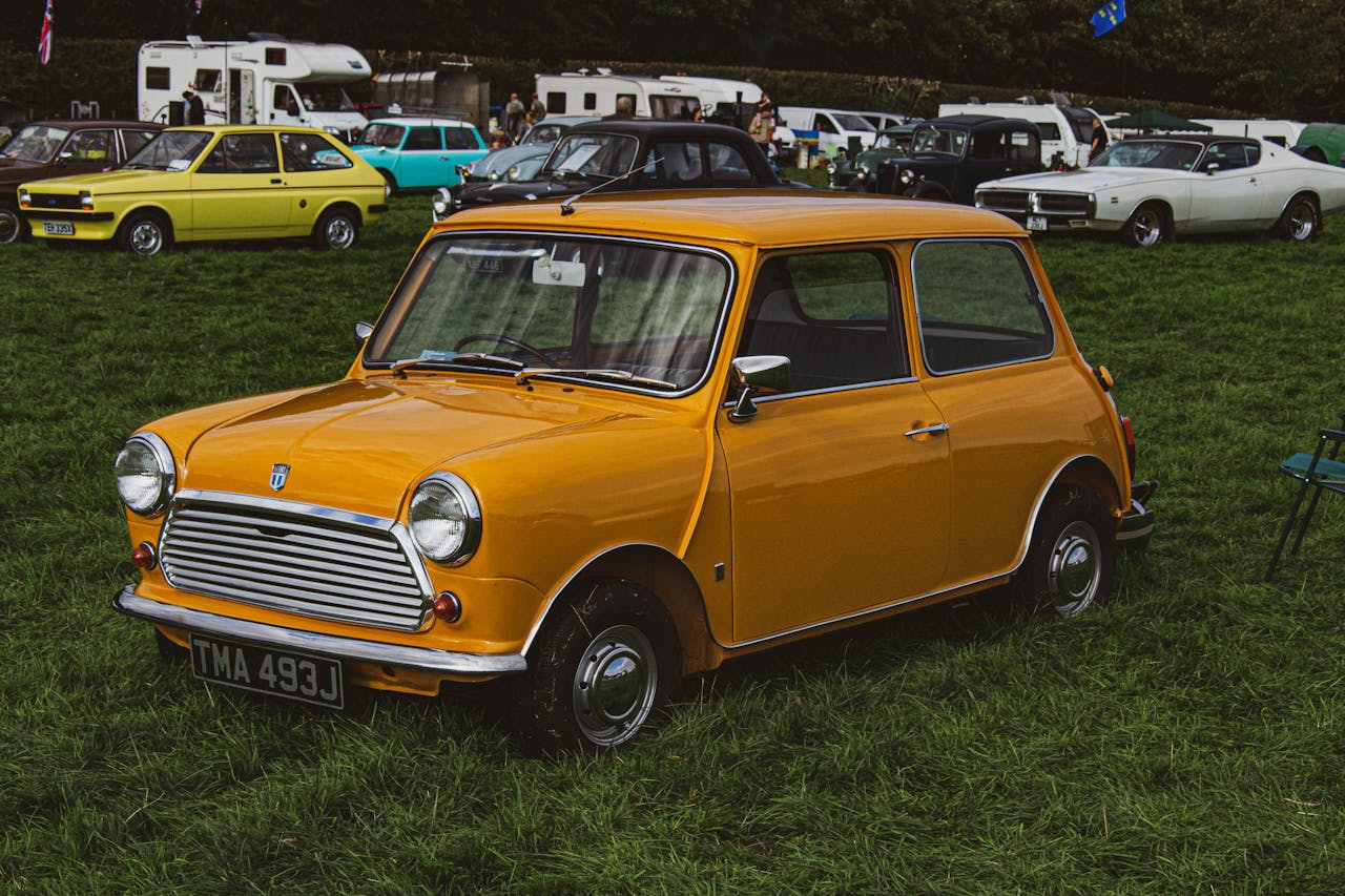 Bright orange vintage Mini car showcased at an outdoor car rally on a grassy field.